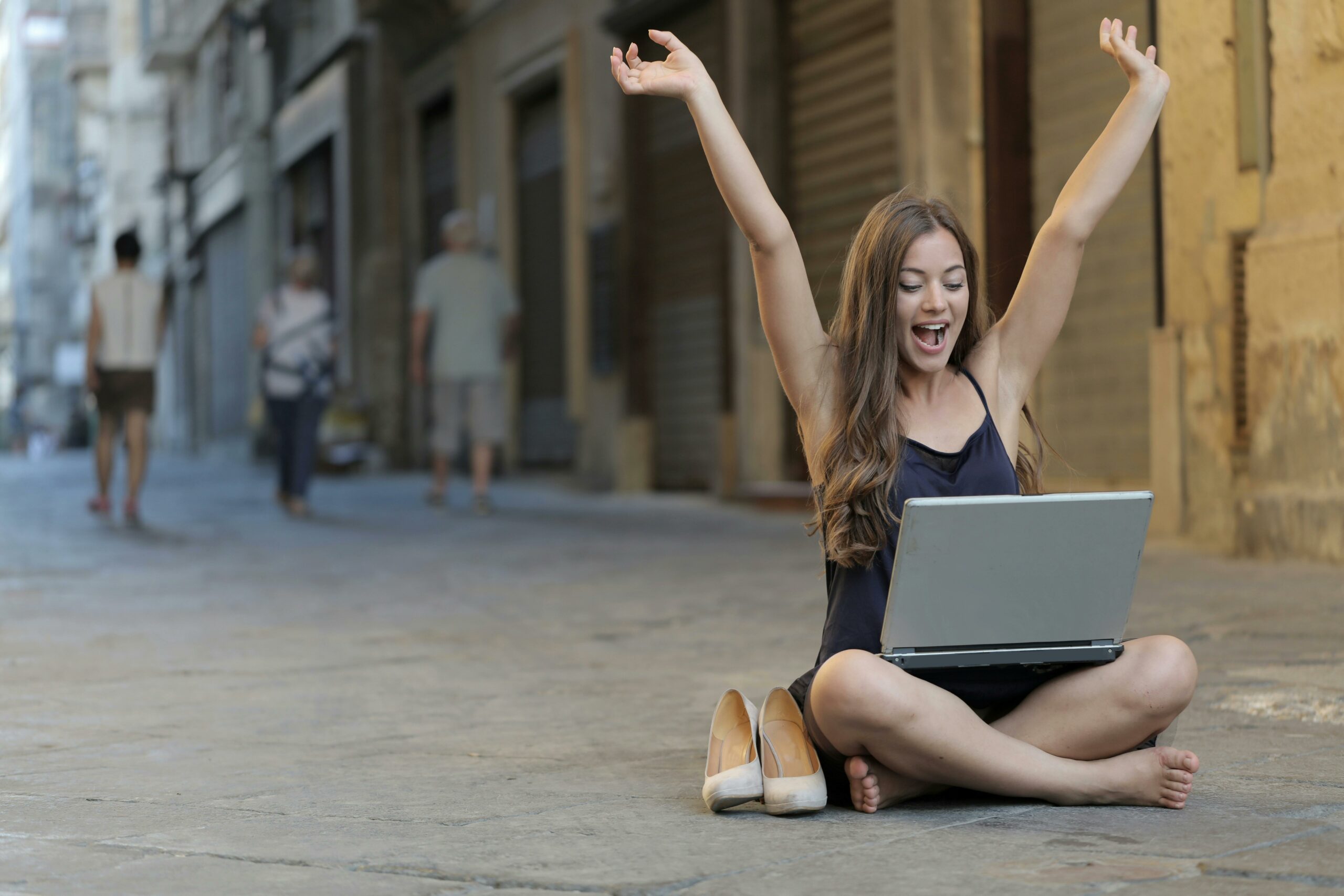 Frau, Die Ihre Hände Beim Sitzen Auf Dem Boden Mit Macbook Pro Auf Schoß Anhebt
